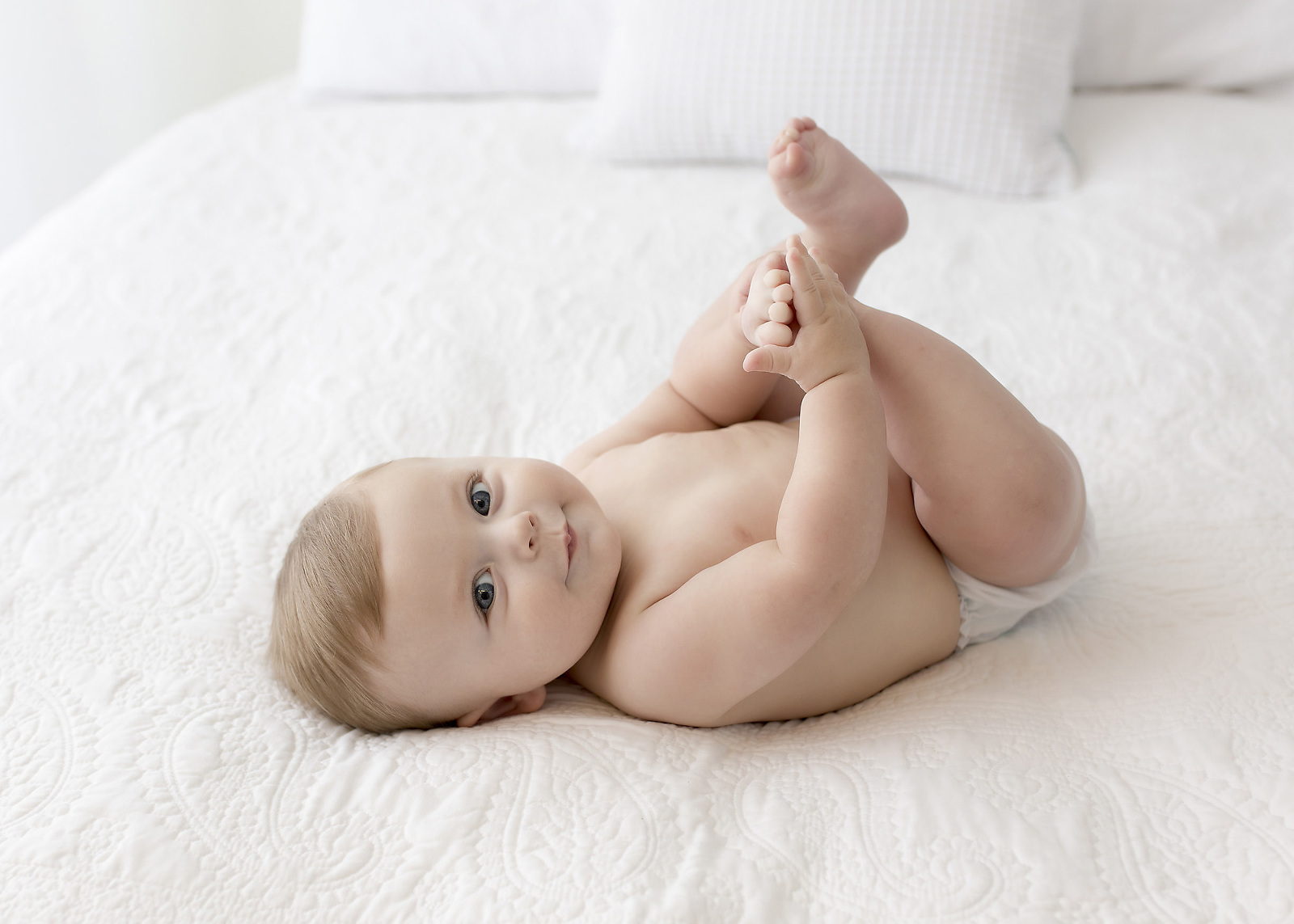 baby laying on back grabbing toes on white bed New Orleans