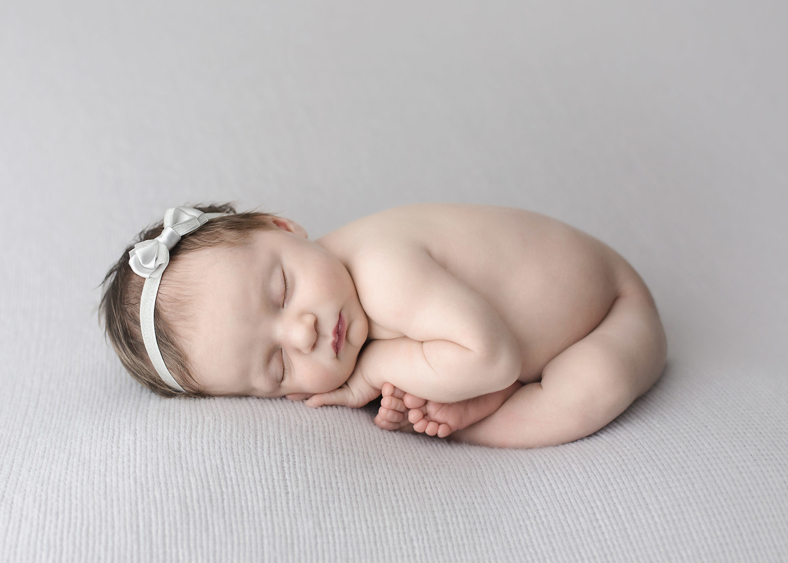 newborn girl naked on gray blanket in womb pose